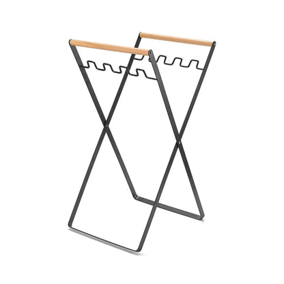 Black iron folding trash rack with wooden handles mounted on a wall holding a recycling bag.