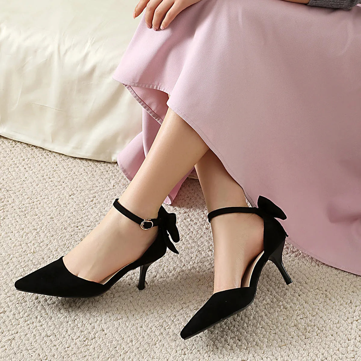 Black stiletto high heels with pointed toe, bowknot detail, and buckle closure on suede upper