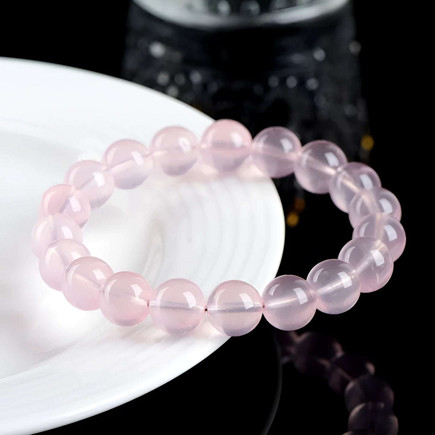 A polished natural starlight crystal round bead bracelet in pink, showing different size options on a wrist.