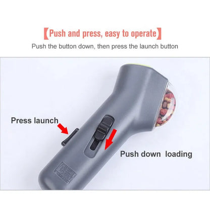 Grey plastic pet snack catapult launcher toy with ergonomic handle, shown with treats.