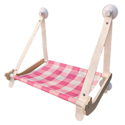 Pink cat hammock with wooden frame and suction cups attached to a window, with a cat resting inside.