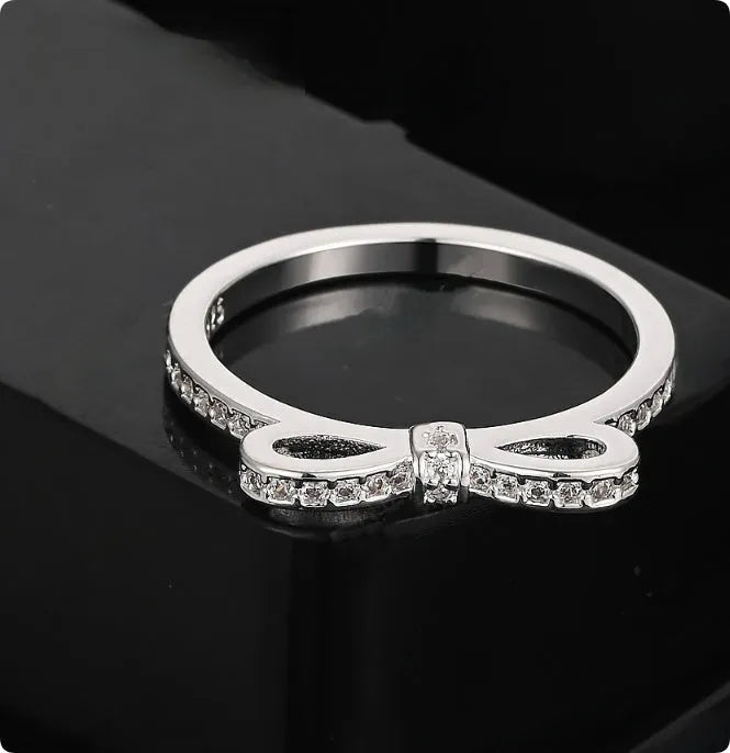 Silver bow-shaped ring with zircon crystal accents on finger, showing electroplated finish and detailed bow design