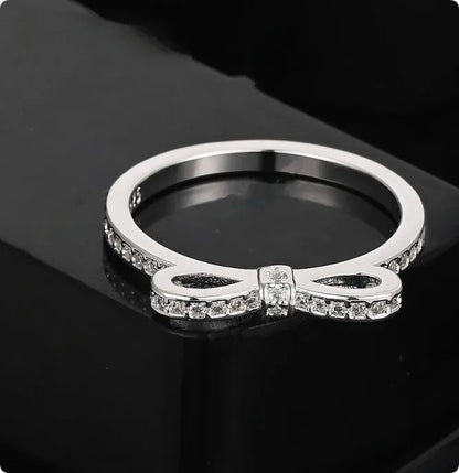 Silver bow-shaped ring with zircon crystal accents on finger, showing electroplated finish and detailed bow design