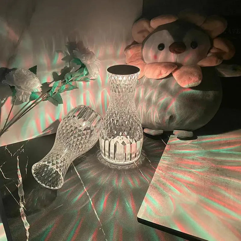 Transparent vase-shaped crystal table lamp with remote control on a wooden bedside table.