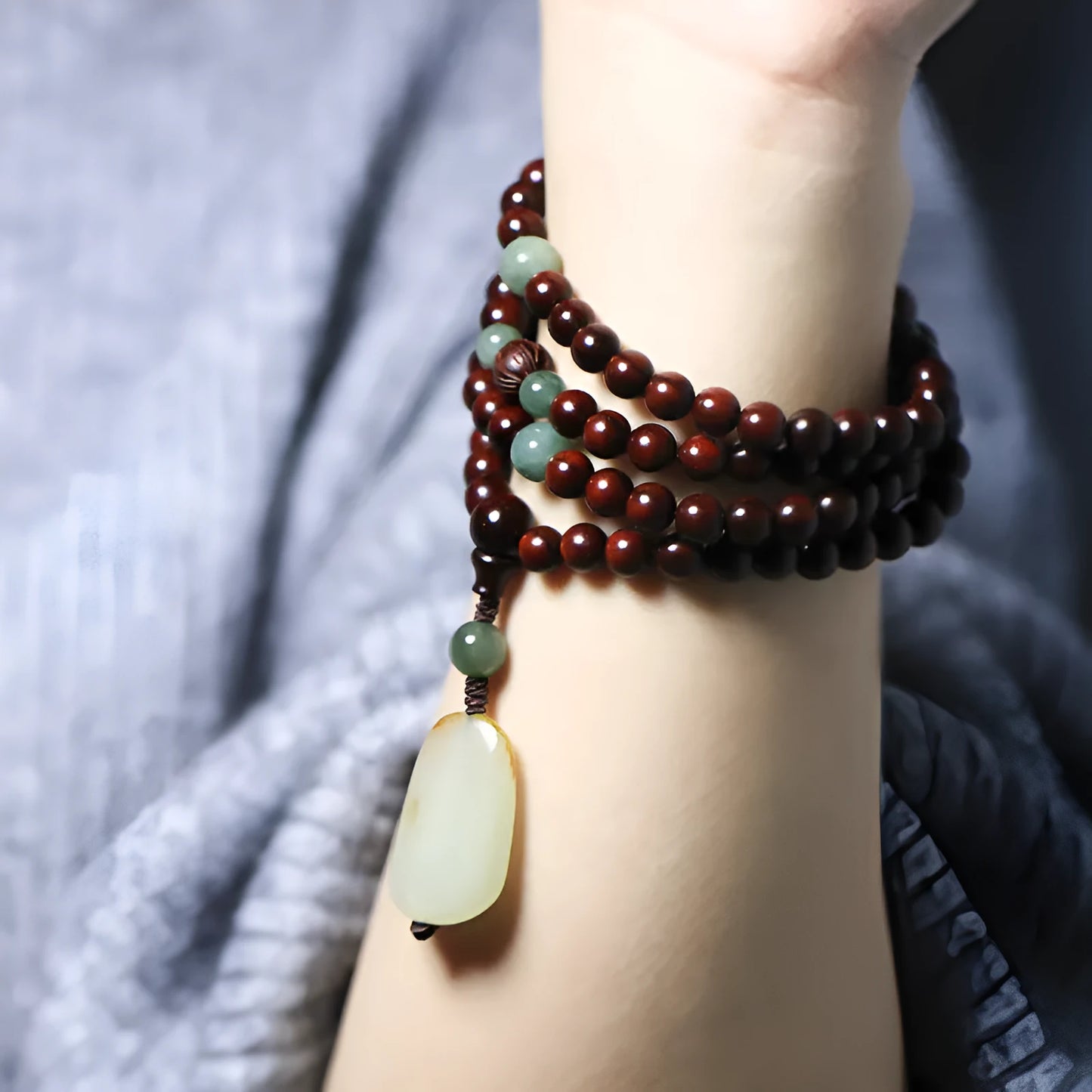 Rosewood bead bracelet with a carved wooden 108 bead and a green Hotian jade pendant on a neutral background.