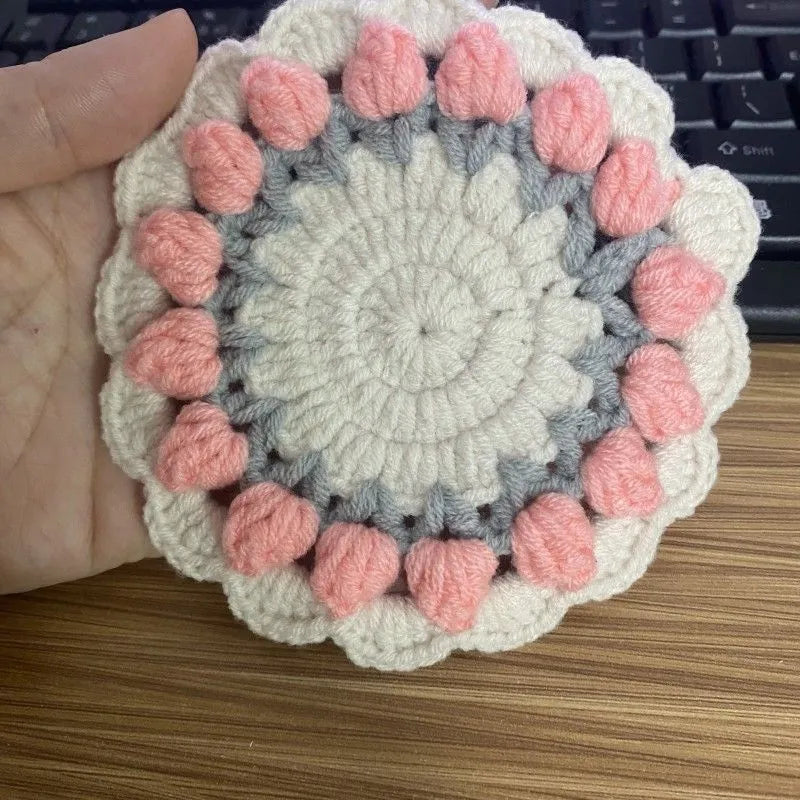 Handmade woven flower coaster in cotton and linen on a wooden table.