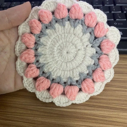 Handmade woven flower coaster in cotton and linen on a wooden table.