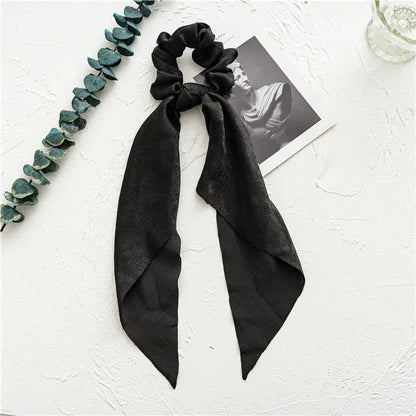 Long dark green cloth ribbon hair tie threaded through a large silver metal ring, laid flat on a surface.