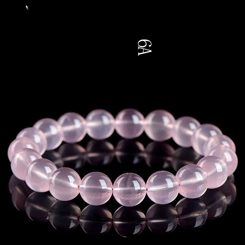 A polished natural starlight crystal round bead bracelet in pink, showing different size options on a wrist.