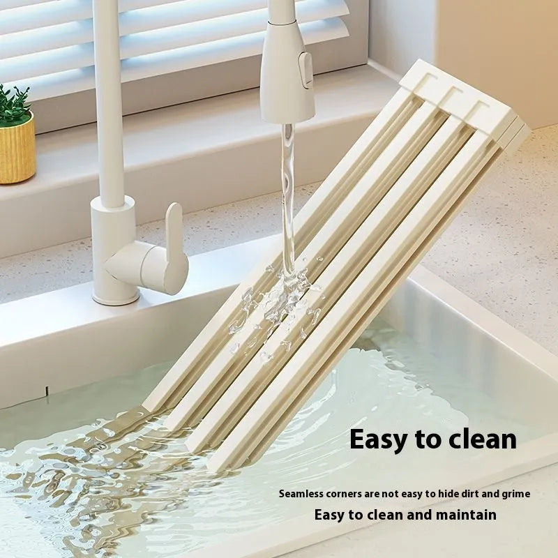 A milky white foldable stainless steel kitchen draining rack collapsed flat beside a kitchen sink.
