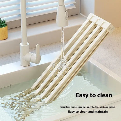 A milky white foldable stainless steel kitchen draining rack collapsed flat beside a kitchen sink.