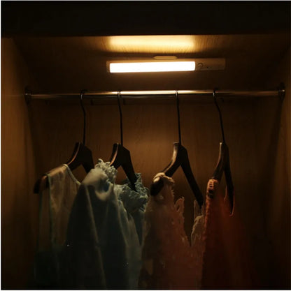 Slender white human body induction LED cabinet light with magnetic back for tool-free installation.