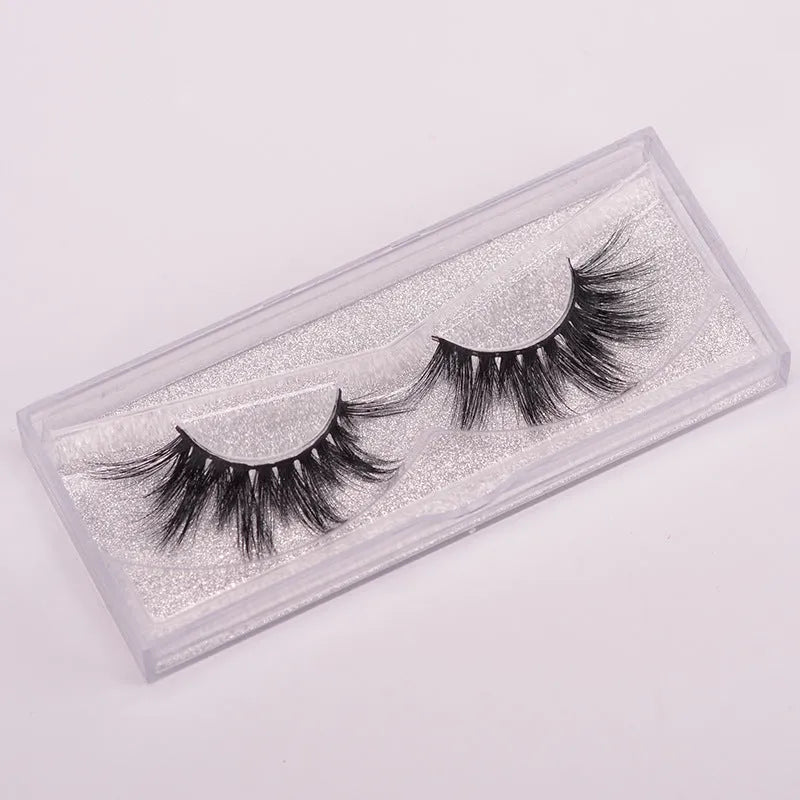 A pair of 5D mink false eyelashes with a hair storage cap and double-ended brush on a pink background.