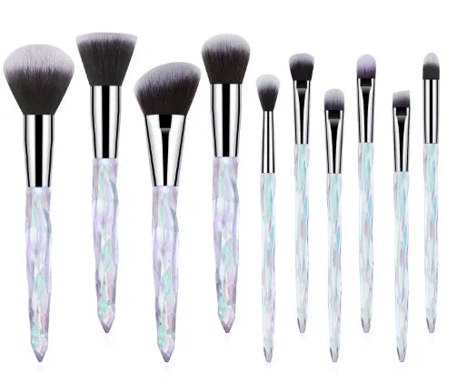 Ten clear crystal-handled foundation brushes with black synthetic bristles laid out on a surface.