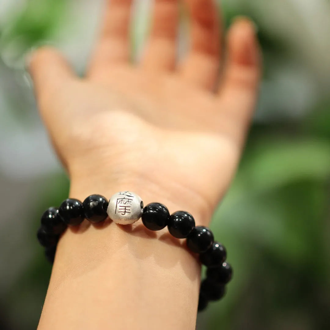 A bracelet with large black agate beads and a sterling silver clasp on a wrist.
