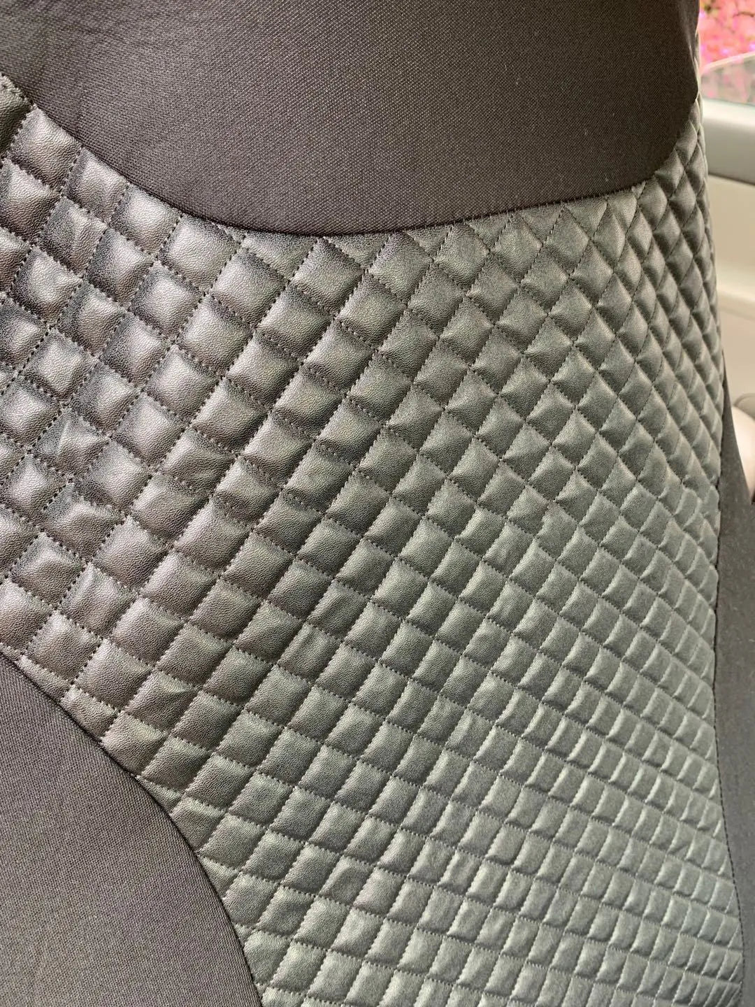 Black quilted universal car seat cover fitted on a front car seat, showing diamond stitching and plastic hook fastenings.