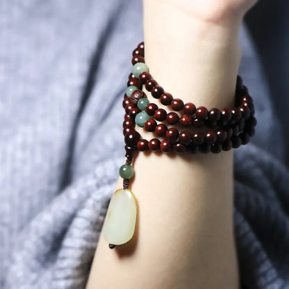 Rosewood bead bracelet with a carved wooden 108 bead and a green Hotian jade pendant on a neutral background.