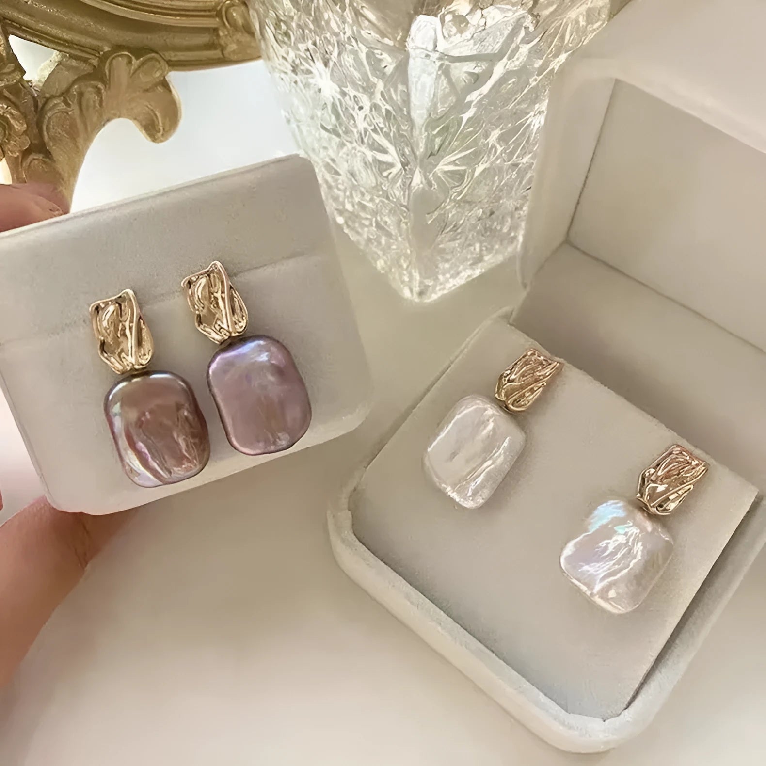 A pair of square stud earrings with a natural freshwater pearl in a geometric alloy setting.