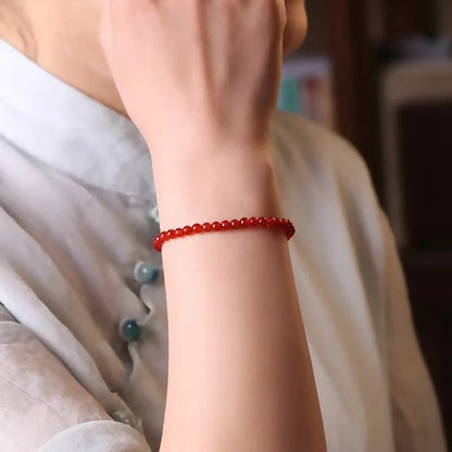 Slim red agate bead bracelet for women on a wrist, classic minimalist jewellery style.