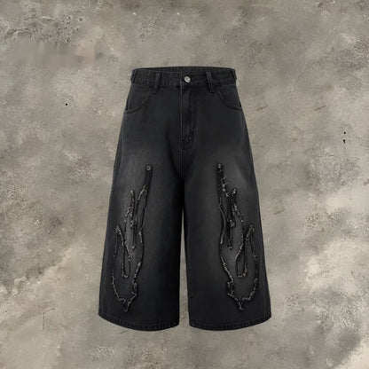 Men's black denim shorts with a cropped flame embroidery patch on the leg.