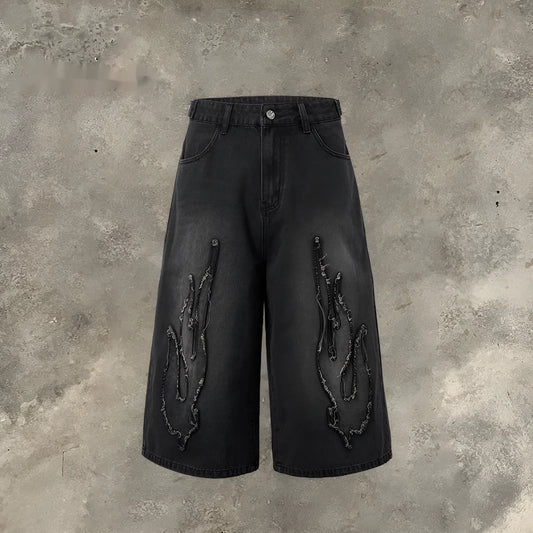 Men's black denim shorts with a cropped flame embroidery patch on the leg.