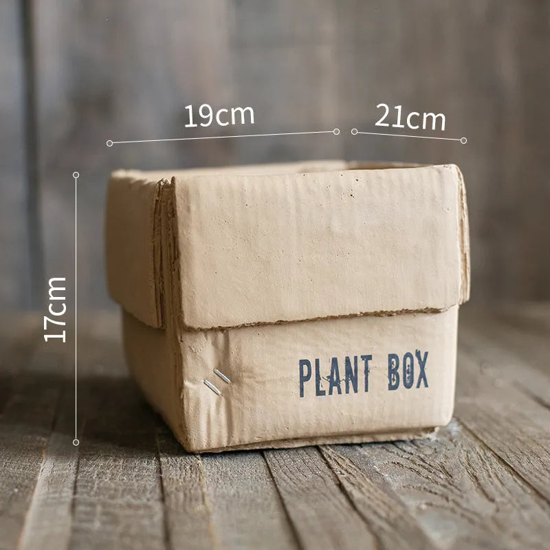 Square cement planter with matte finish and drainage holes, next to a small green plant.