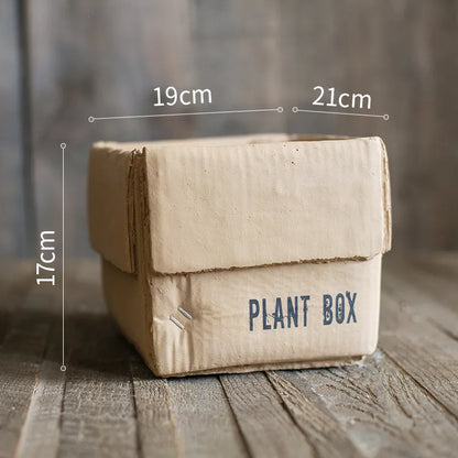Square cement planter with matte finish and drainage holes, next to a small green plant.