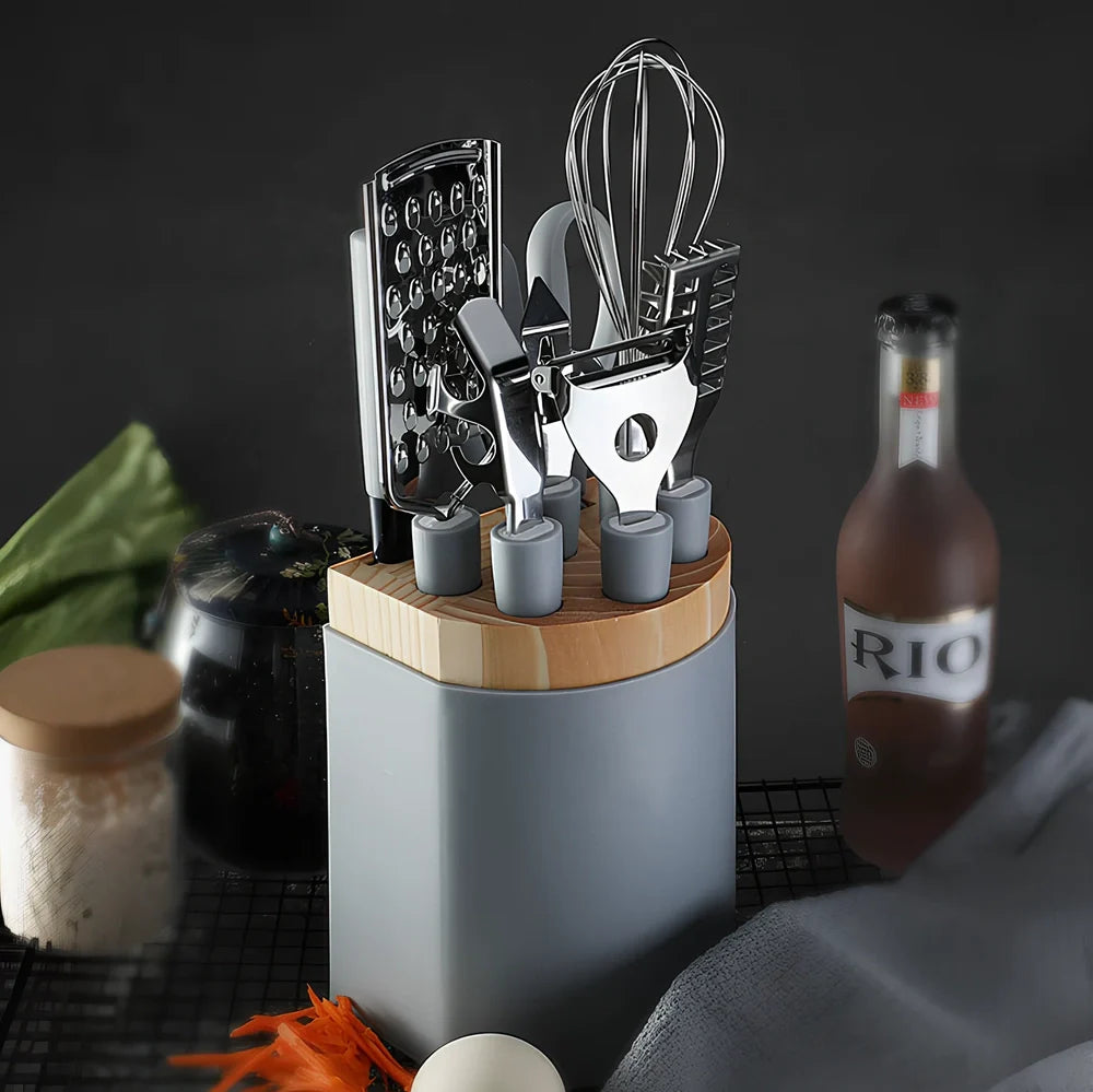 Stainless steel kitchen utensil set with whisk, grater, peeler, scissors and other tools on grey background