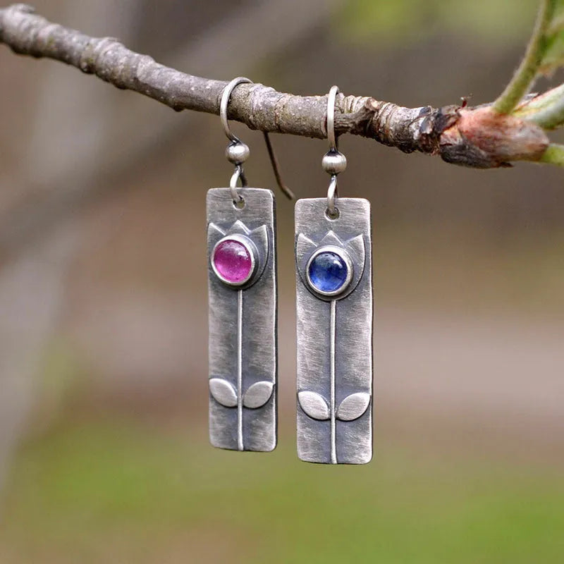 Geometric ellipse-shaped antique finish earrings with red sapphire stones on a white background.