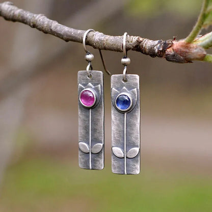 Geometric ellipse-shaped antique finish earrings with red sapphire stones on a white background.