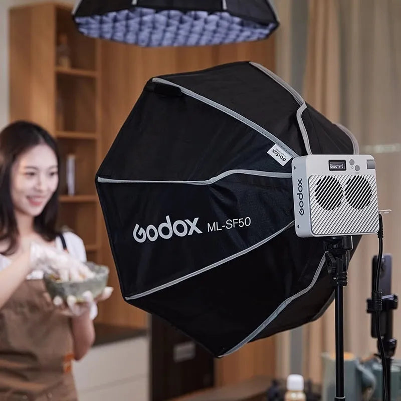Shenniu ML100Bi 200W LED photography fill light with lenses, battery handle, and accessories on a studio table.