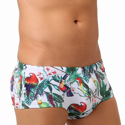 Men's blue swimming trunks with a detailed floral and bird print pattern, shown in a brief style.