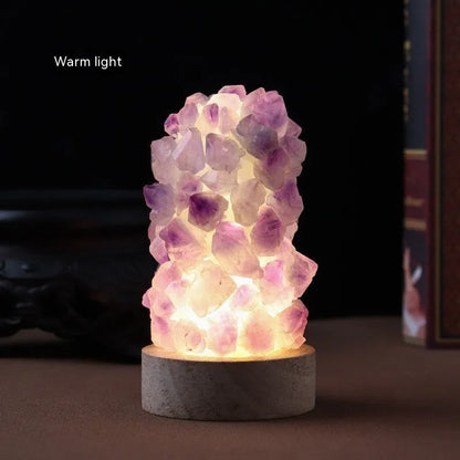 Miniature amethyst crystal tooth flower night light glowing with warm light on a wooden surface.
