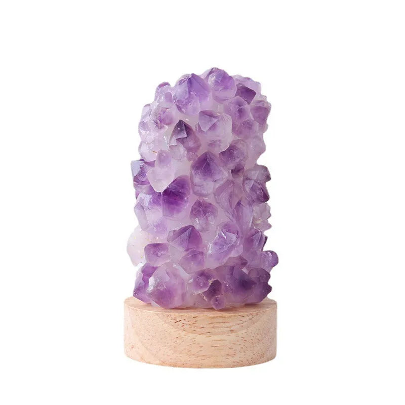 Miniature amethyst crystal tooth flower night light glowing with warm light on a wooden surface.