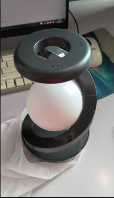 A rotating moon-shaped desk lamp with a wireless charging pad for smartphones, featuring a sleek and modern design.