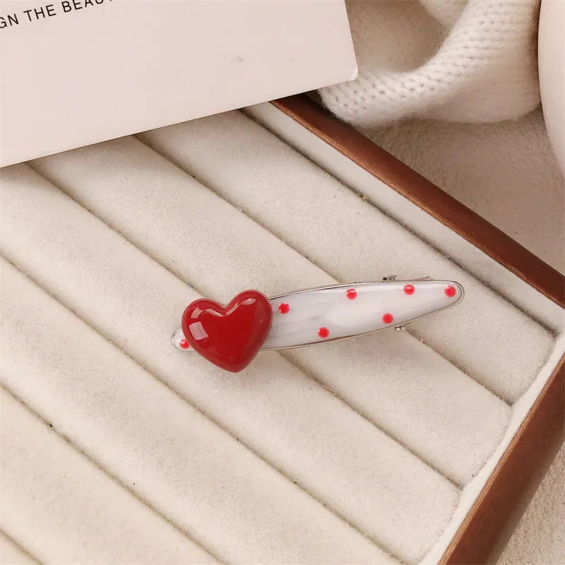 Red plastic hair clip with a 3D love heart and dots on a willow leaf-shaped base.