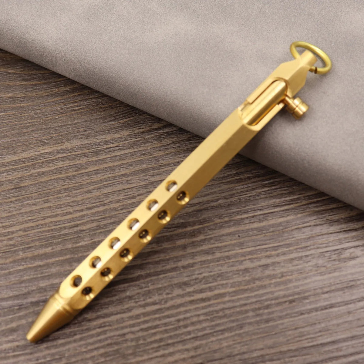 Brass tactical pen with press bolt mechanism showing cylindrical design and six ring details