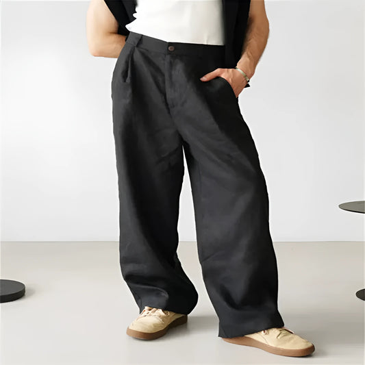 Man wearing loose grey linen blend pleated trousers with a high elasticated waist and straight leg.