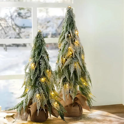 Small green artificial Christmas tree with white snowy branches and built-in warm white lights on a desktop.