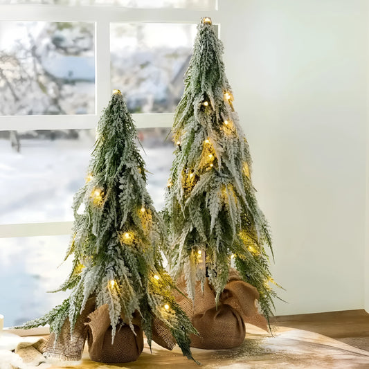 Small white artificial Christmas tree on a table with LED lights and a snow sprayer unit at its base.