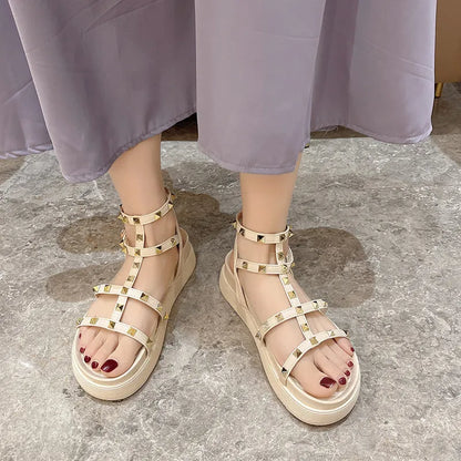Women's Roman-style flat sandals with round toe, rivet platform, ankle buckle, PU upper, rubber sole, beige or black.
