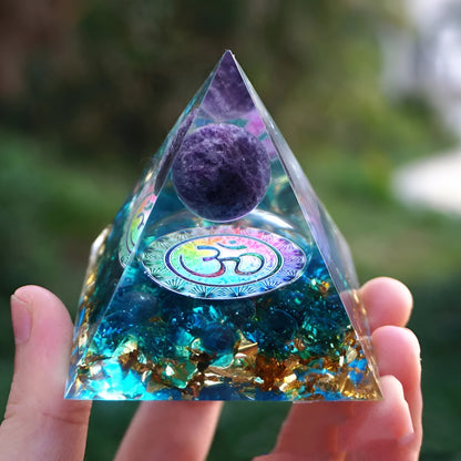 A small 6cm clear epoxy resin pyramid ornament containing pieces of natural crystal gravel on a flat surface.