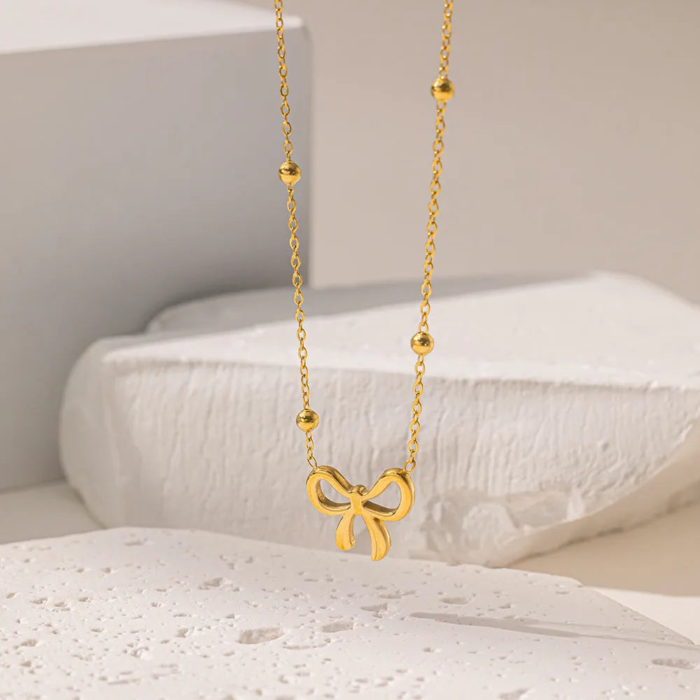 Gold titanium steel necklace with bow pendant on an adjustable cross chain, length 41cm to 50cm.