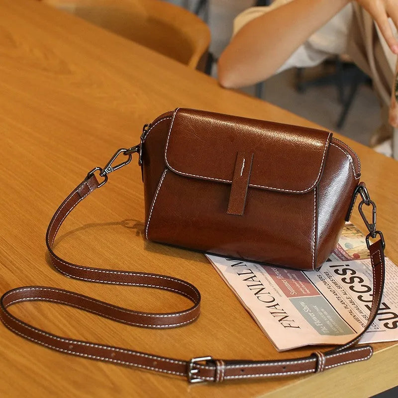 Women's brown shell-shaped genuine leather messenger bag with a single shoulder strap and visible stitching.
