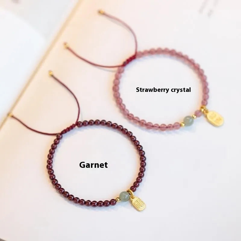 A hand-woven red rope bracelet with a strawberry quartz or garnet crystal, shown in simple styling.