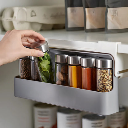 White plastic hanging spice rack with six clear glass bottles, mounted on kitchen door for punch-free storage
