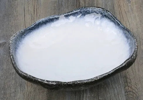 Japanese style irregular shaped ceramic sashimi bowl with floral decoration on table.