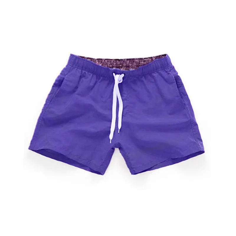 Man wearing straight-leg polyester beach shorts in a bright colour on the sand.