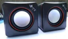 Black square USB computer speaker measuring 10cm with matte finish beside monitor