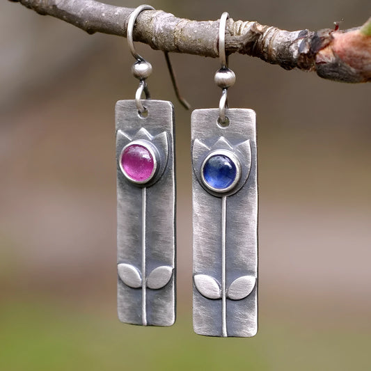 Geometric ellipse-shaped antique finish earrings with red sapphire stones on a white background.